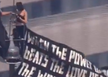Two masked climbers on the Empire State Building antenna holding a power of love banner