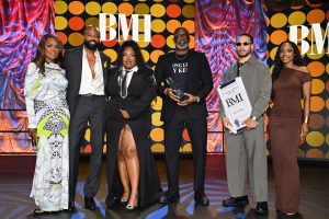 Group of six people on a stage posing for a photo at an awards event, with a bold polka-dot backdrop and BMI lettering behind them.