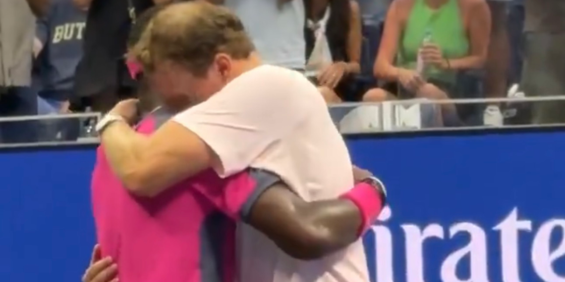 Two athletes embrace in a hug at a sports event, with spectators behind a blue barrier.