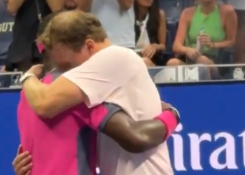Two athletes embrace in a hug at a sports event, with spectators behind a blue barrier.