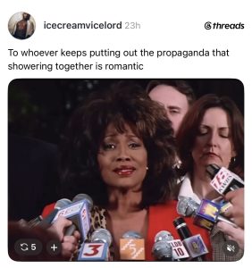 Black woman in a red blazer speaks at a press conference, surrounded by reporters and multiple microphones.