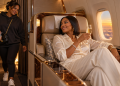 Woman relaxing in first class as her friend walks up from the back of the plane, illustrating the Savannah James first class debate