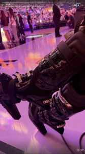 Close-up of black patent DSQUARED2 combat boots with metal buckles, worn at a crowded, pink-lit dance floor.