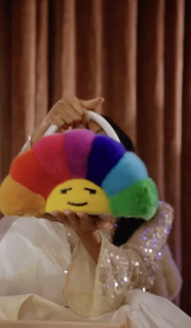Person holding a rainbow-colored plush toy with a yellow smiling sun in the center.